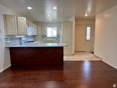 Kitchen featuring a peninsula, a textured ceiling, light wood finished floors, white appliances, and light countertops