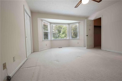 Primary bedroom features a textured ceiling, carpet, a ceiling fan, bay window, and a walk-in closet