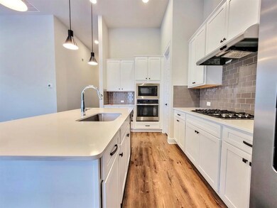 Kitchen featuring white cabinetry, tasteful backsplash, stainless steel appliances, pendant lighting, and under cabinet range hood