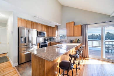 Kitchen featuring tasteful backsplash, light stone counters, wood-type flooring, a kitchen island, and stainless steel appliances