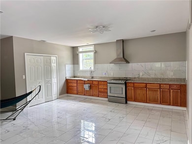 Kitchen featuring wall chimney range hood, stainless steel electric range, a sink, and light marble finish floors