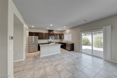 Kitchen featuring dark brown cabinetry, appliances with stainless steel finishes, a kitchen island, light tile patterned floors, and light stone counters