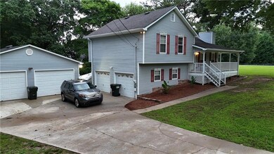 View of front of house featuring a garage, covered porch, a front lawn, a shingled roof, and an outdoor structure