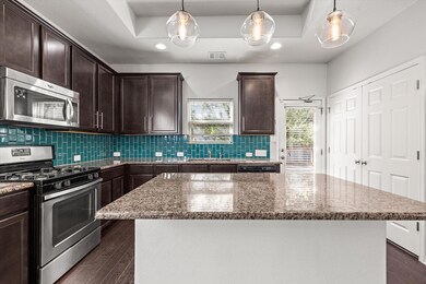 Kitchen featuring appliances with stainless steel finishes, cabinetry, stone countertops, backsplash, and a kitchen island. Double door to the washer and dryer closet on the right.