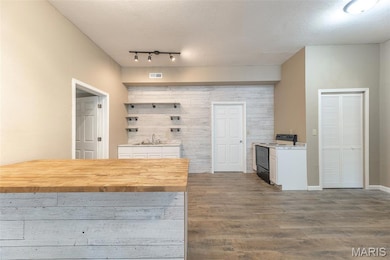 Kitchen with wood finished floors, range with electric stovetop, a textured ceiling, white cabinetry, and a peninsula