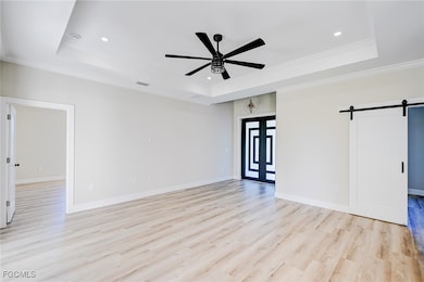 Unfurnished room featuring a barn door, a raised ceiling, light wood-type flooring, recessed lighting, and ornamental molding