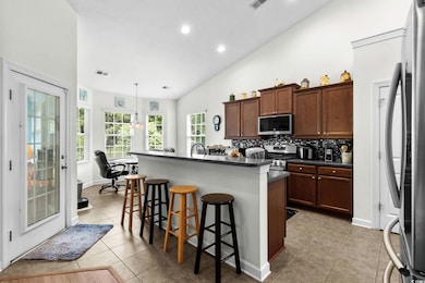 Kitchen featuring a kitchen breakfast bar, stainless steel appliances, light tile patterned flooring, dark countertops, and a kitchen island with sink