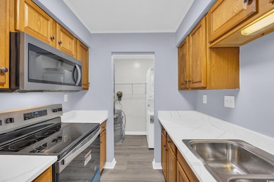 Kitchen featuring appliances with stainless steel finishes, brown cabinets, crown molding, light stone countertops, and light wood finished floors