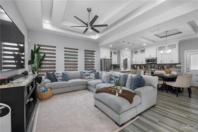 Living area featuring a raised ceiling, ceiling fan, recessed lighting, light wood-style floors, and a chandelier
