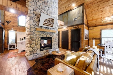 Living area with wood walls, high vaulted ceiling, hardwood / wood-style floors, a stone fireplace, and a wood ceiling with exposed beams