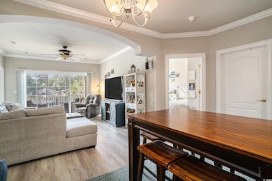 Living room featuring arched walkways, a chandelier, light wood finished floors, a ceiling fan, and crown molding