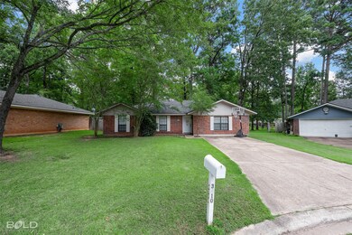 Ranch-style home featuring brick siding, a front lawn, an outdoor structure, driveway, and view of scattered trees