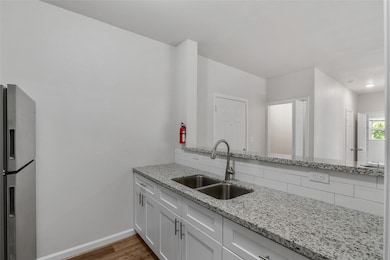 This kitchen features a spacious granite bar countertop that opens up to the living room, perfect for entertaining or casual dining. The double sink is paired with a sleek gooseneck faucet, while the stainless steel refrigerator adds a modern touch to the space. The open layout allows for easy interaction between the kitchen and living area, creating a seamless flow for everyday living. The granite countertops provide both style & functionality, making this space ideal for those who enjoy cooking & hosting