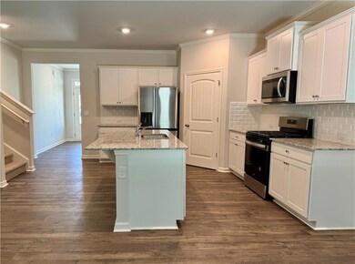 Kitchen featuring stainless steel appliances, light stone counters, white cabinetry, ornamental molding, and dark wood-style flooring