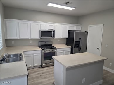 Kitchen with white cabinetry, stainless steel appliances, light countertops, and light wood-style floors