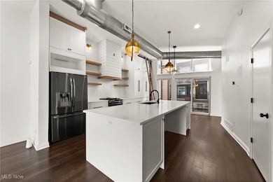 Kitchen featuring pendant lighting, stainless steel fridge, backsplash, dark hardwood floors, and a center island with sink