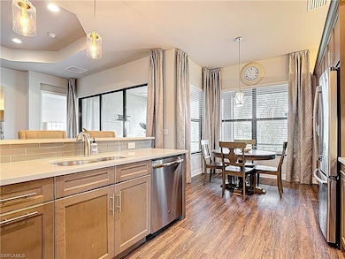 Kitchen featuring stainless steel appliances, dark wood-style flooring, decorative light fixtures, light countertops, and a tray ceiling