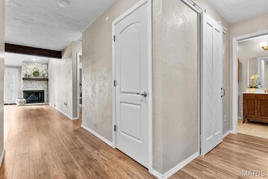Hallway featuring light wood-style floors, beam ceiling, and a textured wall
