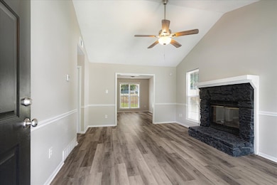 Unfurnished living room with wood finished floors, a stone fireplace, ceiling fan, and high vaulted ceiling