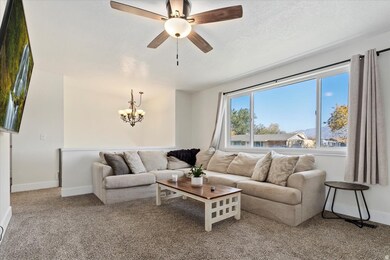 Carpeted living room featuring a ceiling fan, a chandelier, and a textured ceiling