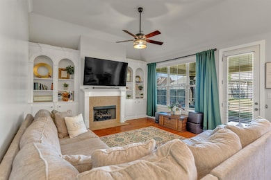 Living room featuring wood finished floors, a tiled fireplace, built in shelves, lofted ceiling, and a ceiling fan