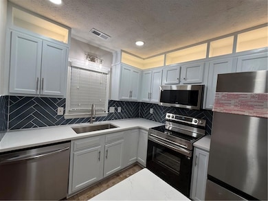 Kitchen featuring paneled fridge, stove, dishwashing machine, a textured ceiling, and tasteful backsplash