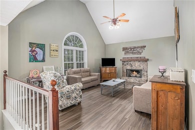 Living room with high vaulted ceiling, a ceiling fan, light wood-style flooring, and a stone fireplace