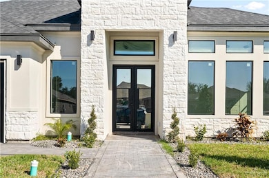 View of exterior entry featuring stone siding, roof with shingles, and french doors