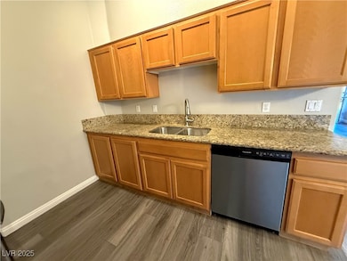 Kitchen with dishwasher, light stone countertops, dark wood-type flooring, and brown cabinets