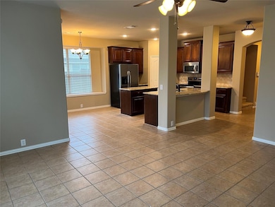 Kitchen with appliances with stainless steel finishes, light tile flooring, ceiling fan with notable chandelier, tasteful backsplash, and a center island