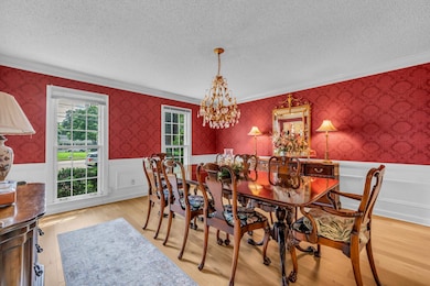 Dining space featuring crown molding, a textured ceiling, wallpapered walls, a chandelier, and a wainscoted wall
