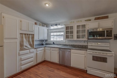 Kitchen featuring appliances with stainless steel finishes, light wood-type flooring, decorative backsplash, glass insert cabinets, and dark countertops