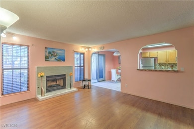 Unfurnished living room with a textured ceiling, light wood-style flooring, a tile fireplace, and arched walkways