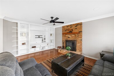 Living room featuring a fireplace, ceiling fan, ornamental molding, and dark wood-type flooring
