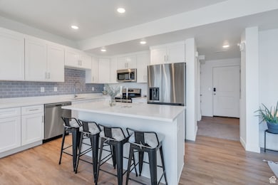 Kitchen with appliances with stainless steel finishes, white cabinetry, decorative backsplash, light wood-type flooring, and a kitchen breakfast bar