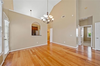 Unfurnished room with high vaulted ceiling, light wood-style floors, a chandelier, baseboards, and arched walkways