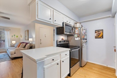 Kitchen featuring white cabinets, stainless steel appliances, light wood-style flooring, and open floor plan