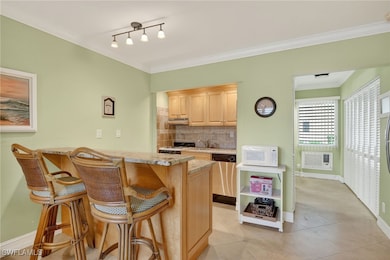 Kitchen with ornamental molding, light brown cabinets, tasteful backsplash, a kitchen bar, and white appliances