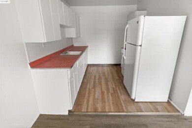 Kitchen with freestanding refrigerator, white cabinets, light wood-style flooring, range, and dark countertops