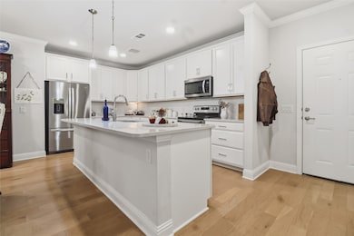 Kitchen with crown molding, white cabinetry, appliances with stainless steel finishes, light wood-style floors, and a kitchen island with sink