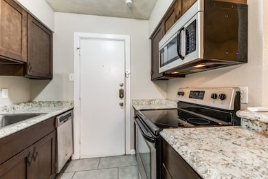Kitchen featuring appliances with stainless steel finishes, light tile patterned flooring, dark brown cabinets, and a textured wall