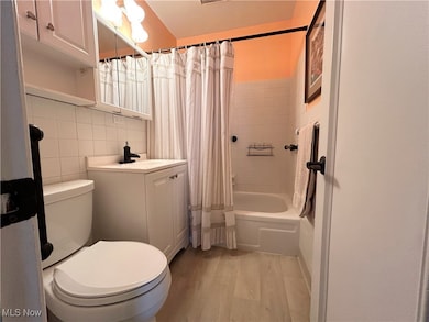 Bathroom featuring light wood-style flooring, vanity, shower / bath combination with curtain, tile walls, and backsplash