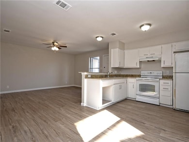 Kitchen featuring white appliances, under cabinet range hood, ceiling fan, white cabinetry, and wood finished floors