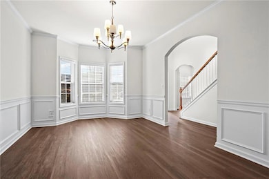 Unfurnished room with a chandelier, arched walkways, dark wood-type flooring, a wainscoted wall, and ornamental molding
