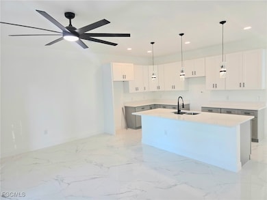 Kitchen with light marble finish flooring, white cabinetry, an island with sink, recessed lighting, and hanging light fixtures