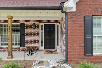 Property entrance featuring brick siding, covered porch, and roof with shingles