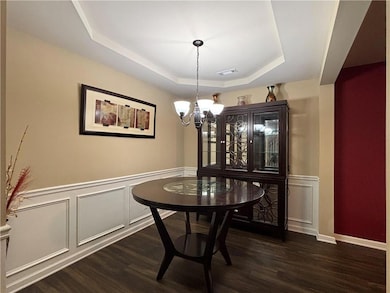 Dining space with a raised ceiling, a chandelier, dark wood-type flooring, wainscoting, and a decorative wall
