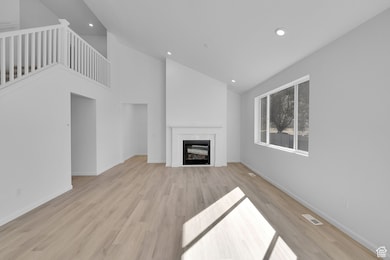 Unfurnished living room featuring light wood-style floors, a glass covered fireplace, high vaulted ceiling, and recessed lighting