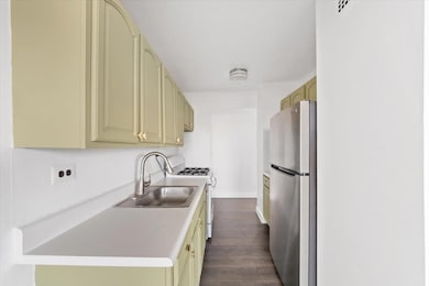 Kitchen featuring dark wood-type flooring, cream cabinetry, a sink, freestanding refrigerator, and white range with gas stovetop