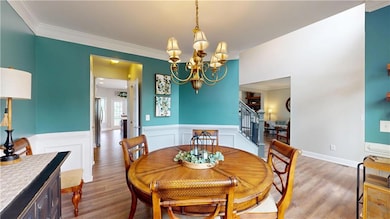 Dining room with stairs, wood finished floors, a chandelier, wainscoting, and ornamental molding